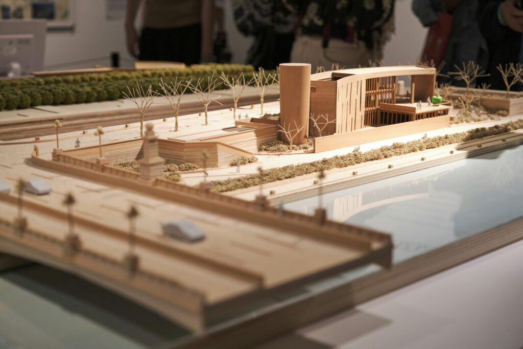 A physical architectural scale model showing a proposed building development, landscaping, and bridge infrastructure used for preconstruction planning.