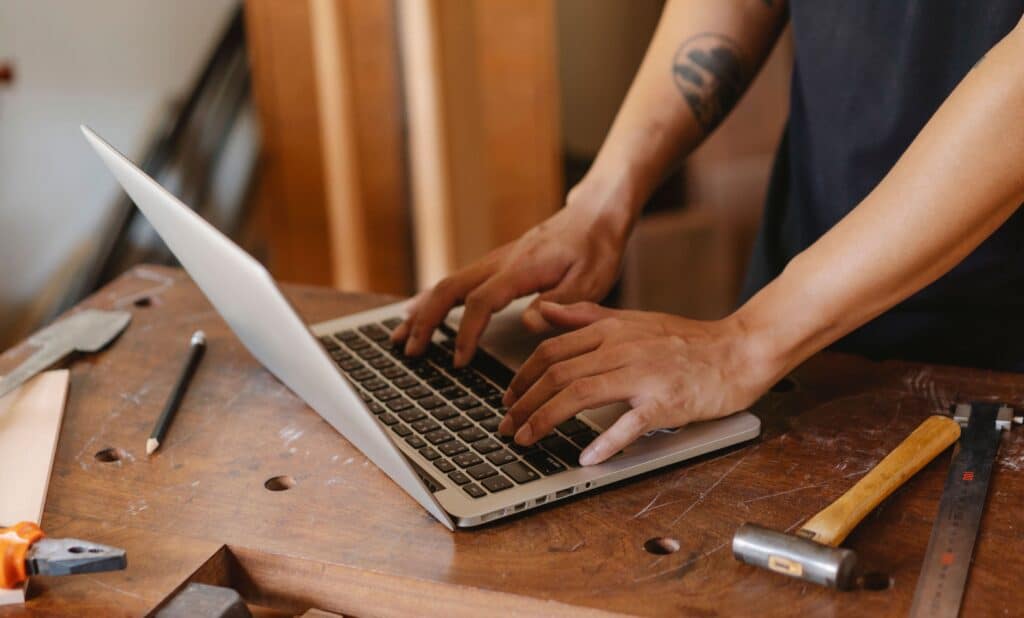 Man using a laptop on his work bench surrounded by tools.