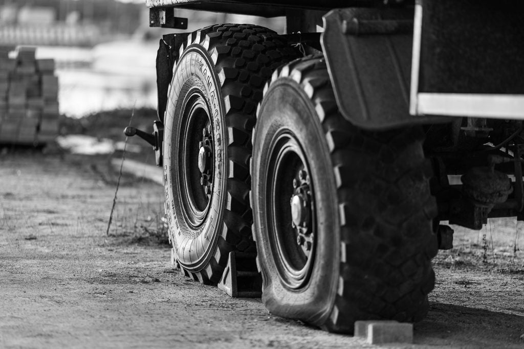 Black and white image of a truck at a construction site with a partially deflated tire.