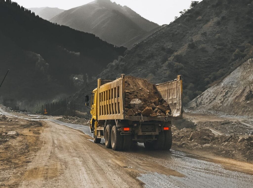 Large yellow truck hauling dirt down an unpaved road.