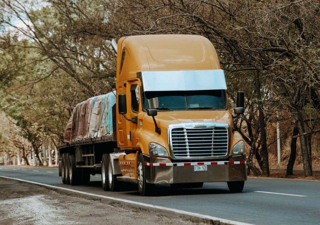 Orange semi carrying tarped materials to construction site.